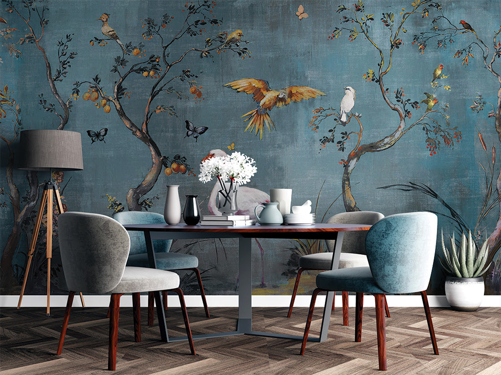 A vibrant mural depicting a whimsical nature scene with flowering trees, birds, butterflies, and a central pink flamingo. The textured blue background enhances the detailed foliage and wildlife, creating a serene and artistic ambiance full of life and color.