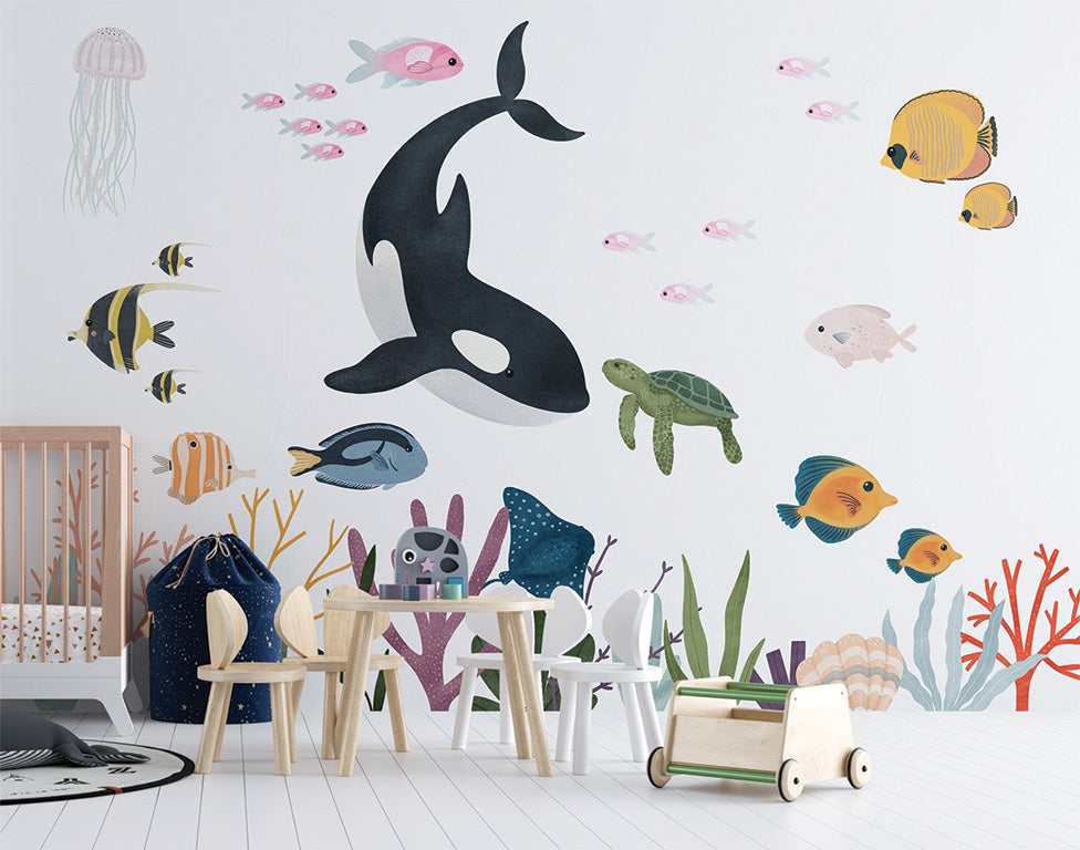 This colorful underwater illustration features a diverse array of marine life, including a playful orca, a sea turtle, various tropical fish, and vibrant coral reefs. A jellyfish and schools of pink fish add dynamic movement to the tranquil background. The scene showcases the beauty of marine biodiversity.