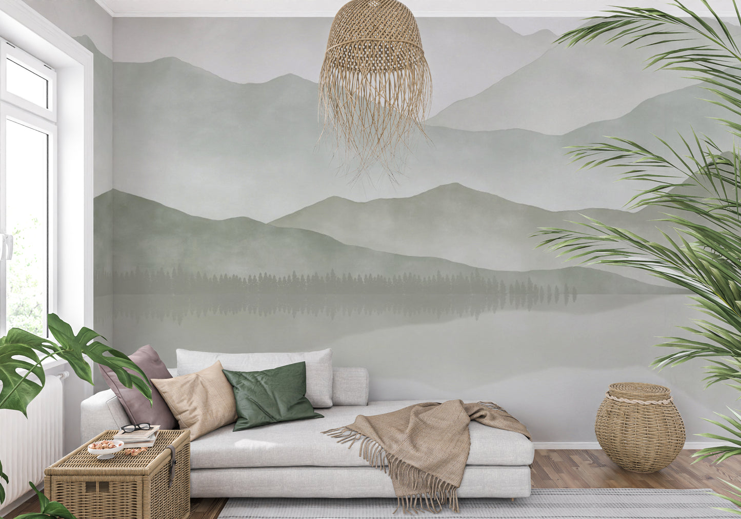 Adrienne - Custom Wallpaper Mural l Wallab Egypt. A serene living room featuring a wall mural of misty mountains and a forest reflected in a lake. The room is furnished with a light grey sectional sofa adorned with green and beige pillows, a wicker coffee table, and a cozy blanket. Natural elements such as large potted plants and a woven pendant light enhance the tranquil, nature-inspired atmosphere. 